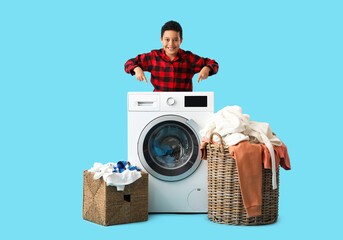 Little African-American boy, washing machine and baskets with laundry on blue background