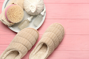 Pair of beige soft slippers and cosmetic products on pink background. Top view