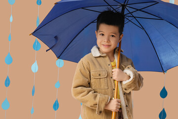 Cute little Asian boy with umbrella and raindrops on beige background