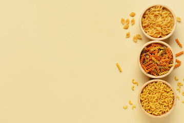 Bowls with different tasty uncooked pasta on beige background