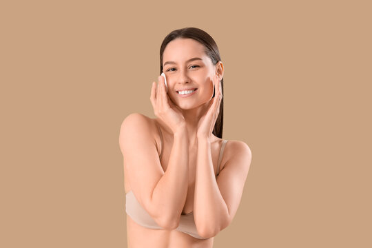 Young woman with cotton pad removing makeup on brown background