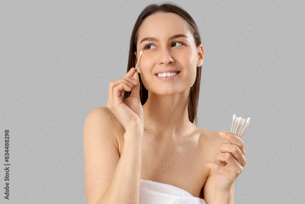 Sticker young woman with cotton buds removing makeup on grey background, closeup