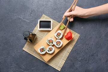 Female hand holding chopsticks with tasty sushi rolls, soy sauce and wasabi on black grunge background