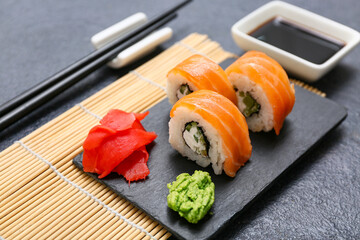 Board with tasty sushi rolls, marinated ginger and wasabi on black grunge background, closeup