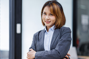 Fototapeta premium Young Asian business woman smiling confidently while standing alone in a bright modern office 