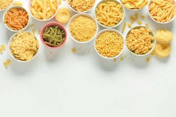Bowls with different raw tasty pasta on white background