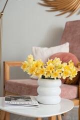 Armchair and coffee table with vase of narcissus flowers and magazine in living room