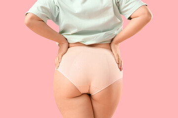 Young woman in period panties on pink background, back view