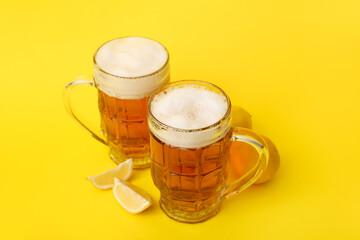 Glasses of fresh beer with lemon on yellow background