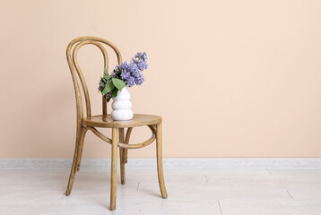 Vase with lilacs branches on chair near beige wall in room
