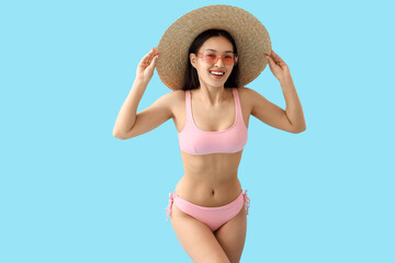 Young Asian woman in pink swimsuit with hat and sunglasses on blue background