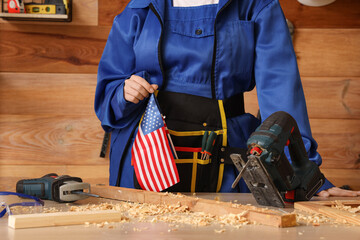 Female carpenter with cordless jigsaw and USA flag in workshop. Labor Day celebration