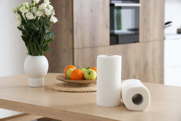 Rolls of paper towels with fruits and flowers on table in kitchen, closeup