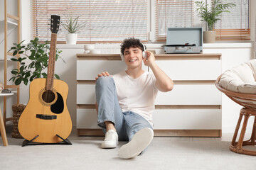Handsome young man in headphones with record player listening to music at home