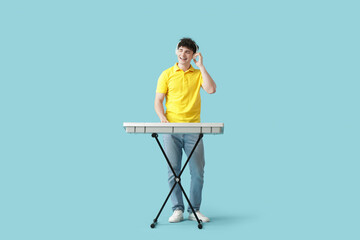 Handsome young man in headphones playing synthesizer on blue background