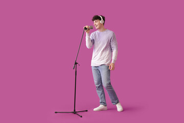 Handsome young man in headphones with microphone singing on purple background