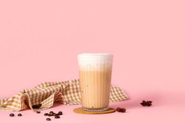 Glass of iced latte with star anise and coffee beans on pink background