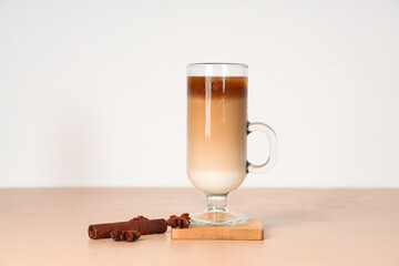 Glass cup of iced latte with cinnamon and star anise on beige table