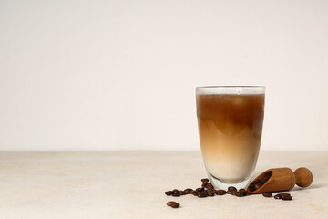 Glass of iced latte and wooden scoop with coffee beans on white background
