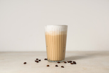 Glass of iced latte and coffee beans on white background