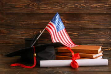 Diploma with books, mortar board and flag of USA on wooden background