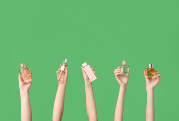 Female hands with different bottles of perfume on green background