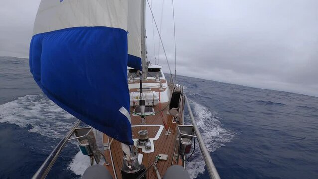 A sailboat is sailing in the ocean with a blue and white flag on the mast. The flag is waving in the wind, and the boat is moving through the water. The scene is peaceful and serene, with the boat