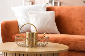 Basket with golden watering can on wooden coffee table in living room, closeup