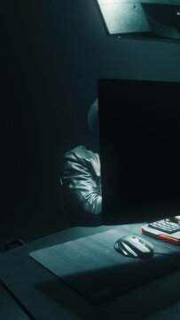 Concept cyber attack of a masked hacker breaking into a corporate data servers from his underground hideout, the place has a dark atmosphere, multiple screens. Vertical shot.