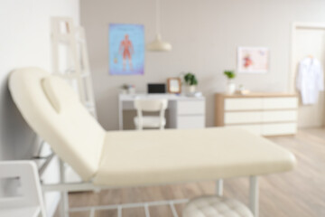 Blurred view of medical office with couch, shelf unit and doctor's workplace