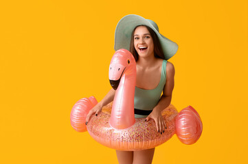 Beautiful young woman in stylish swimsuit with inflatable ring in shape of flamingo on yellow...