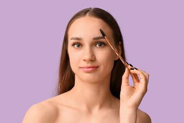 Young woman correcting shape of her eyebrows on lilac background