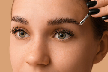 Young woman correcting shape of her eyebrows on brown background, closeup