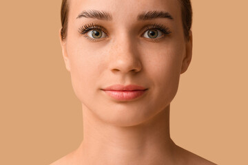 Young woman with beautiful eyebrows on brown background, closeup
