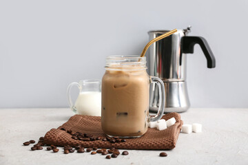 Mason jar of iced latte with coffee beans and cubes of sugar on white background