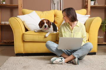 Young woman with Beagle dog using laptop on floor at home