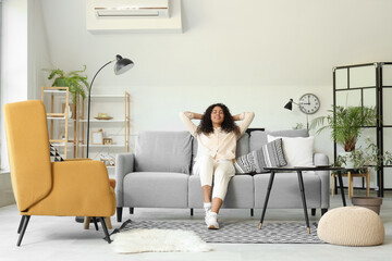 Young African-American woman sitting on grey sofa at home