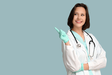 Beautiful female doctor with stethoscope pointing at something on blue background