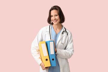 Beautiful female doctor with folders on pink background