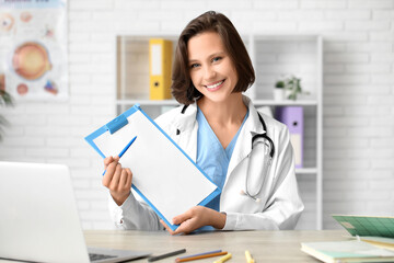 Beautiful female doctor with clipboard at table in clinic