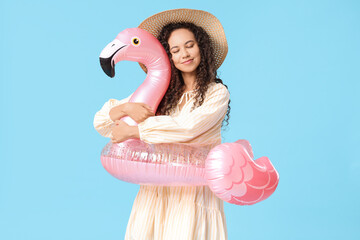 Beautiful young African-American woman with inflatable ring in shape of flamingo on blue background © Pixel-Shot