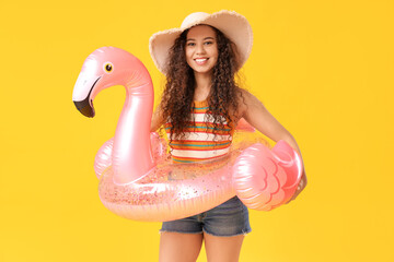 Beautiful young African-American woman with inflatable ring in shape of flamingo on yellow background © Pixel-Shot