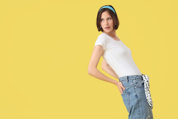 Beautiful young woman in stylish jeans on yellow background