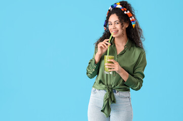 Beautiful young happy African-American woman with glass of tasty kiwi smoothie on blue background