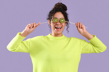 Beautiful young happy African-American woman holding sticks with kiwi on purple background