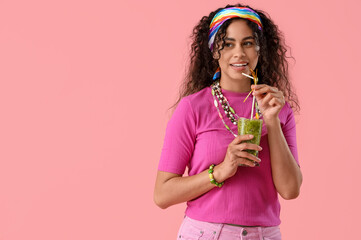 Beautiful young happy African-American woman with glass of tasty kiwi smoothie on pink background