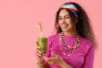 Beautiful young happy African-American woman with glass of tasty kiwi smoothie on pink background