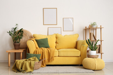 Soft sofa, basket with plaid and cushion, frames on wall and plants in living room
