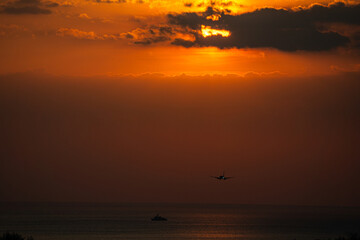 Back view silhouette of airplane landing at the airport at sunny orange and purple sunset. Runway