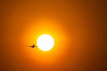 Back view silhouette of airplane take-off into sunny orange and purple sunset